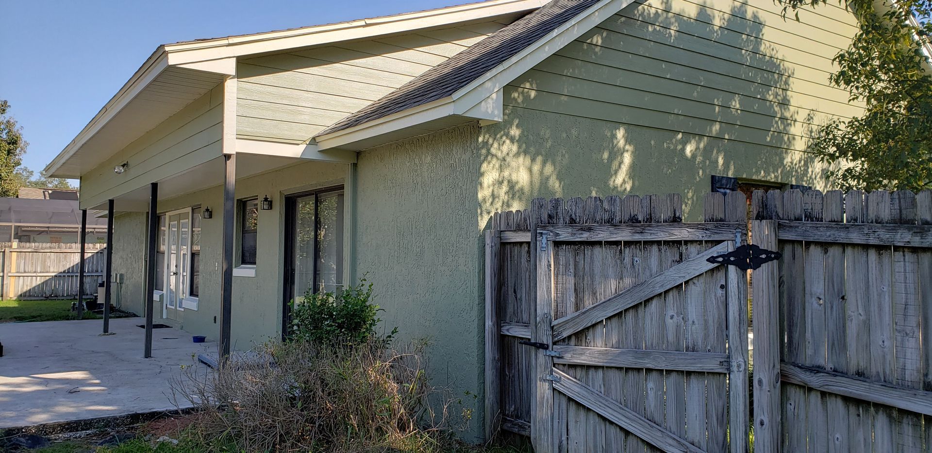 A green house with a wooden fence in front of it.