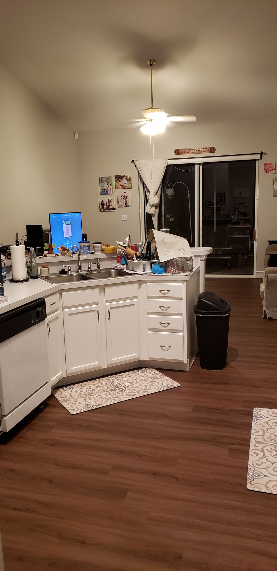 A kitchen with white cabinets , a black dishwasher , and a ceiling fan.