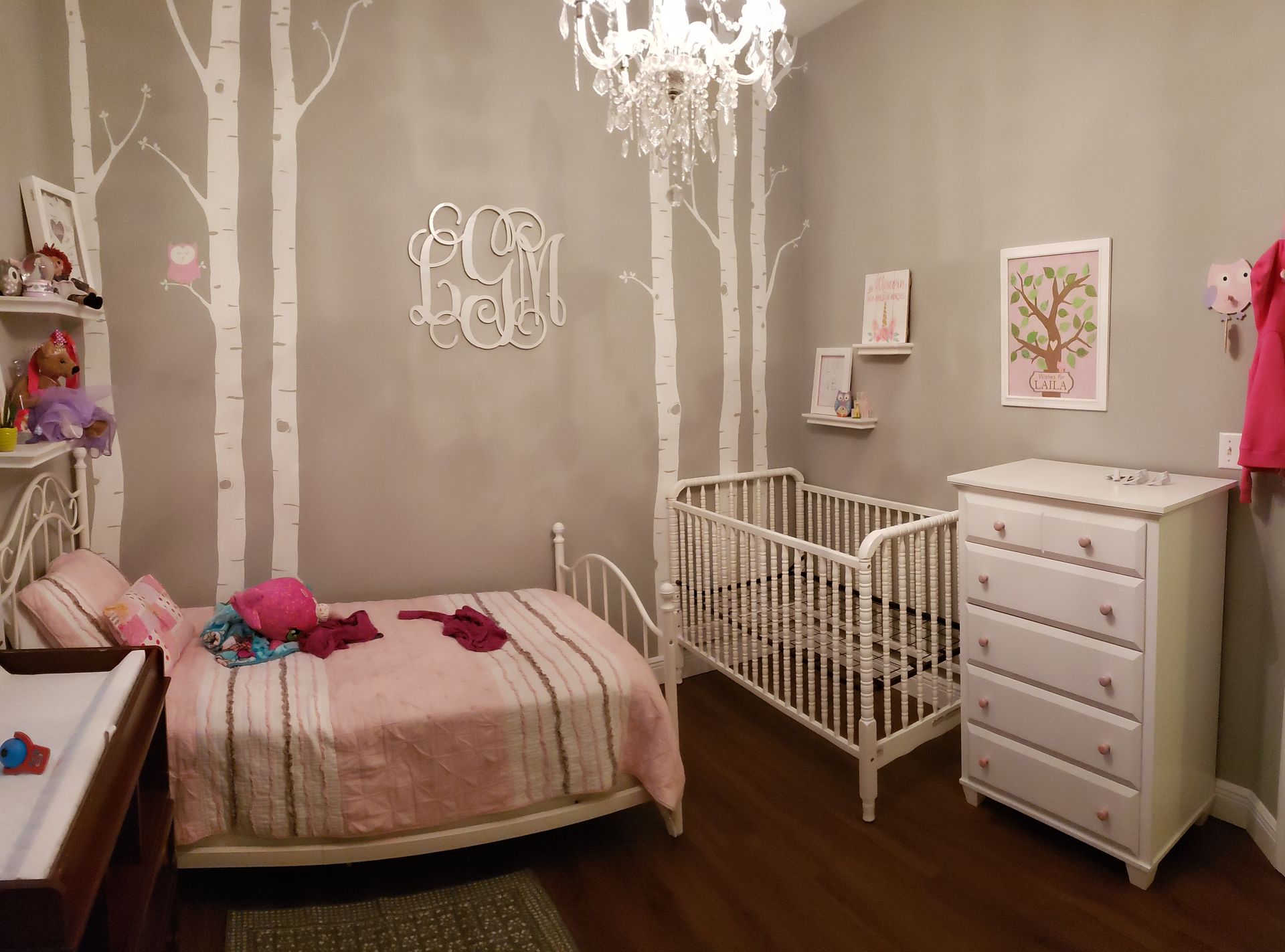 A bedroom with a bed , crib , dresser and chandelier