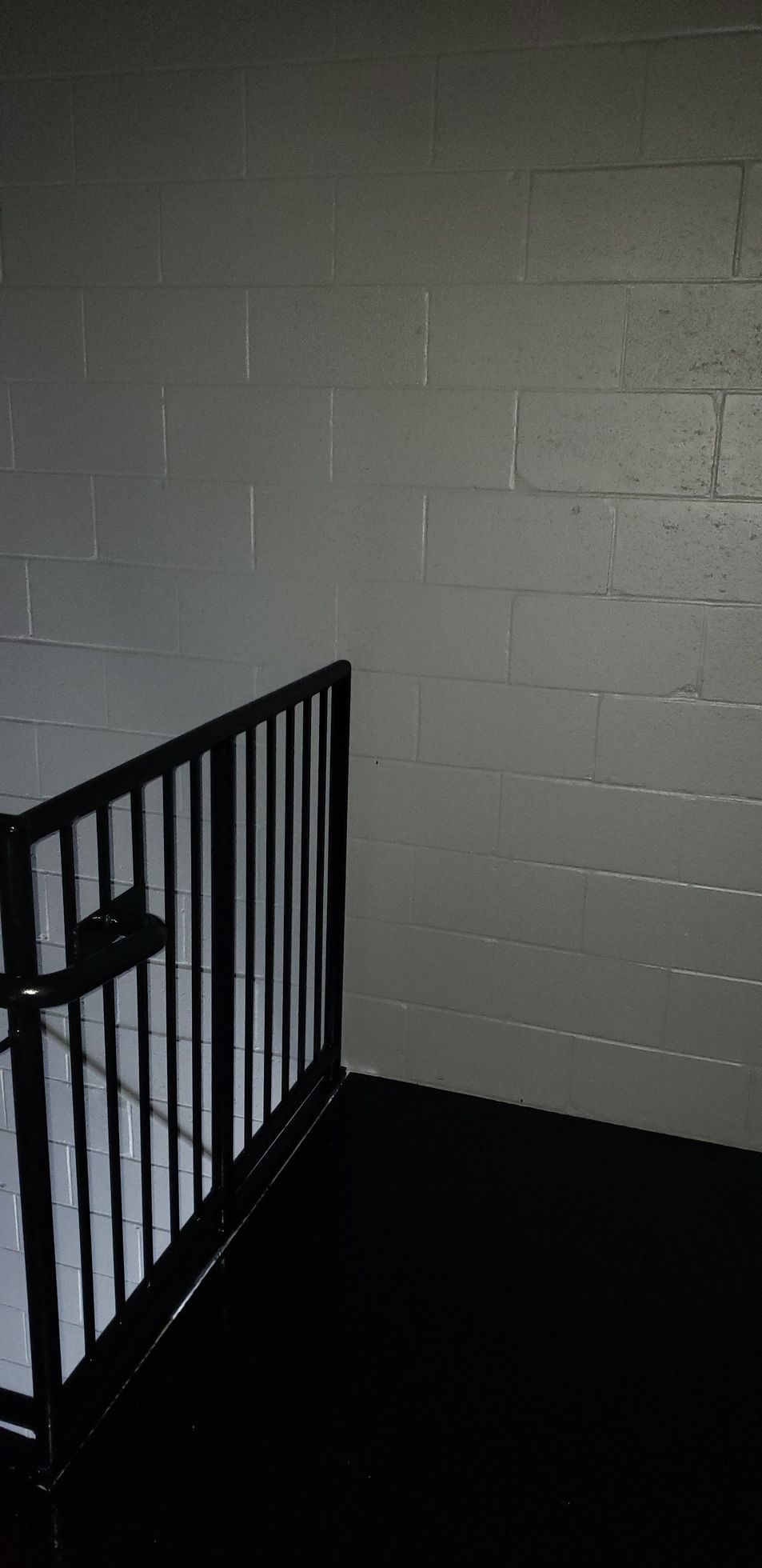 A staircase with a black railing and a white brick wall.