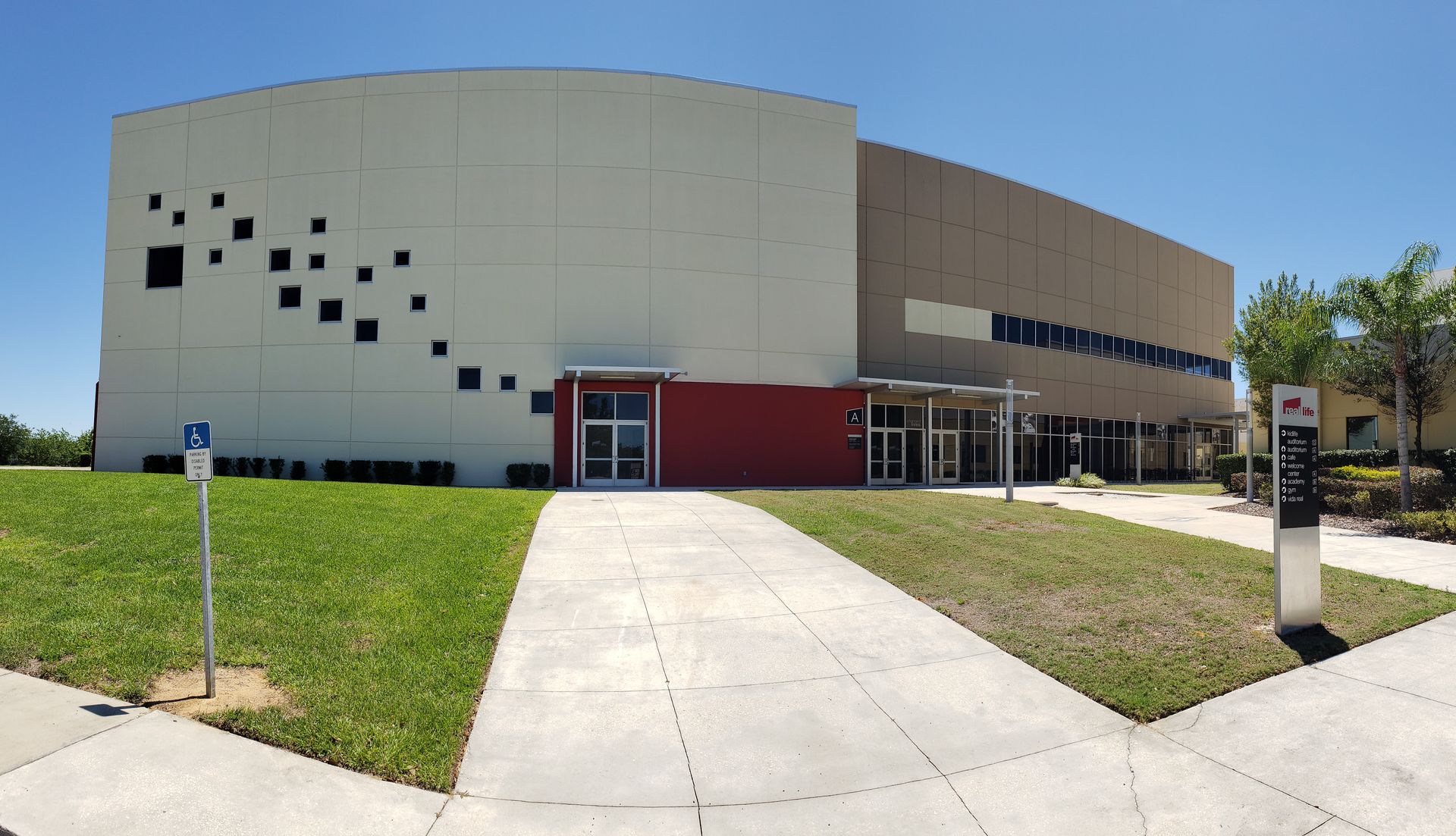 A large white building with a red roof is surrounded by grass.