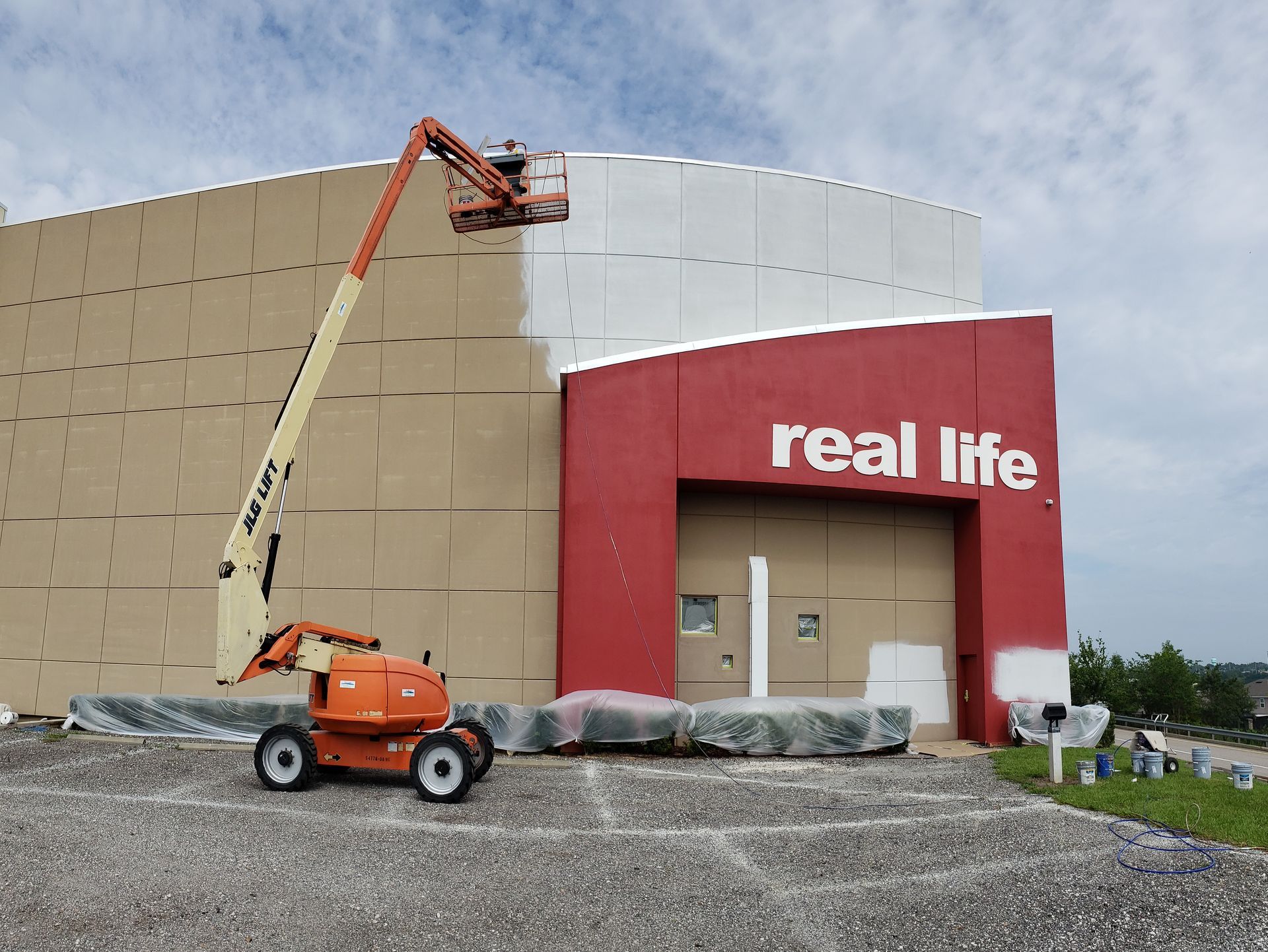 A crane is painting the side of a building that says real life.