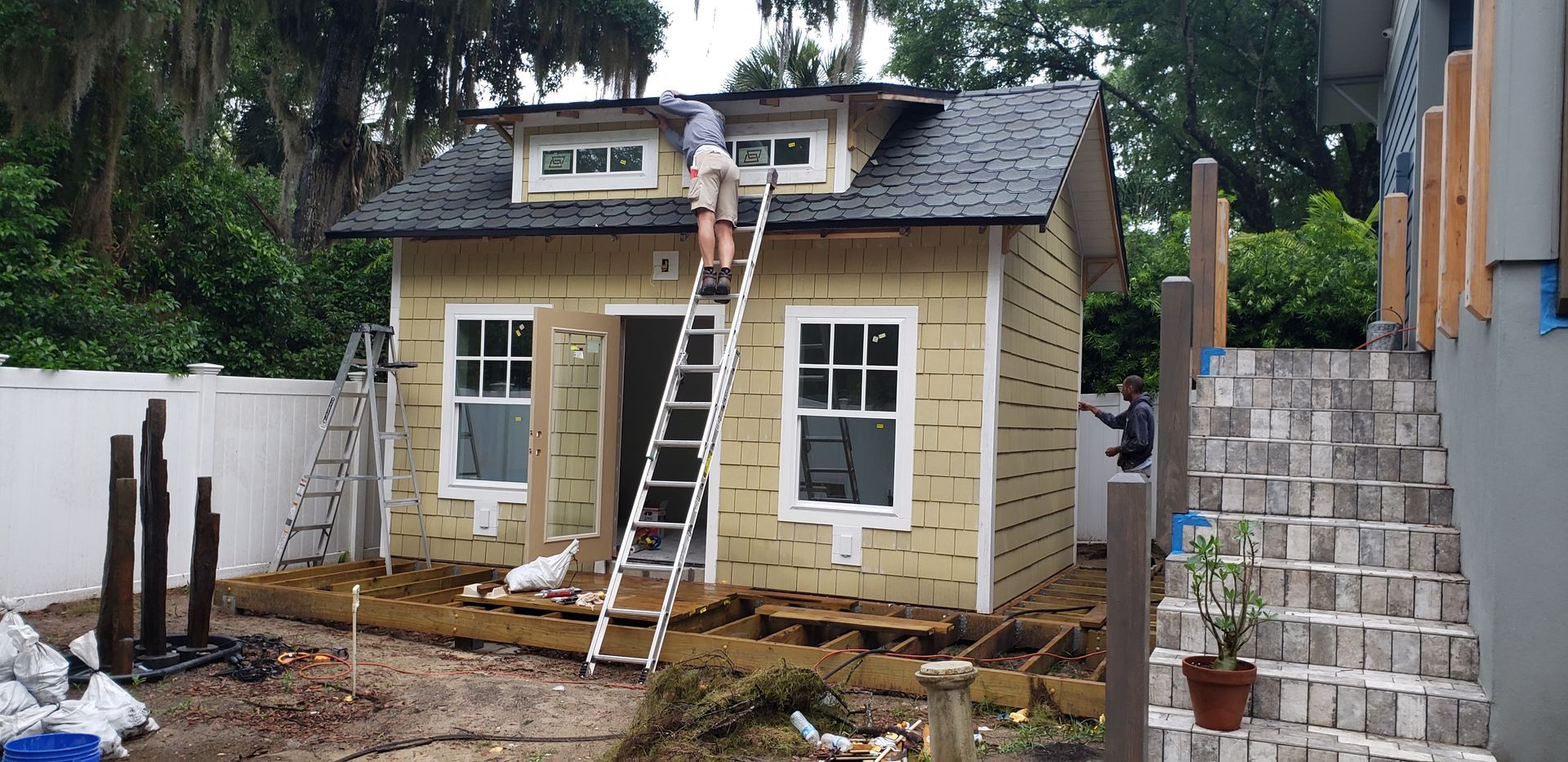 A man on a ladder is working on the roof of a small house.