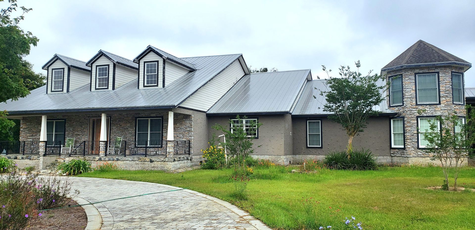 A large house with a metal roof is surrounded by grass and trees