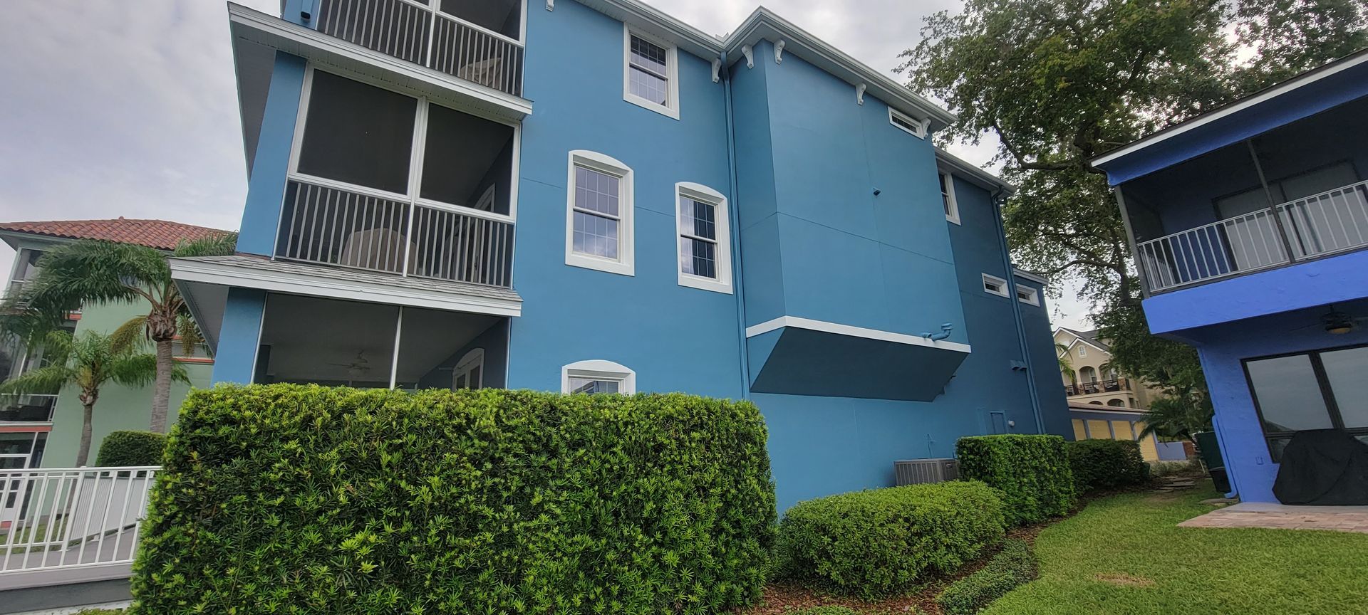 A blue building with a screened in balcony and a hedge in front of it.