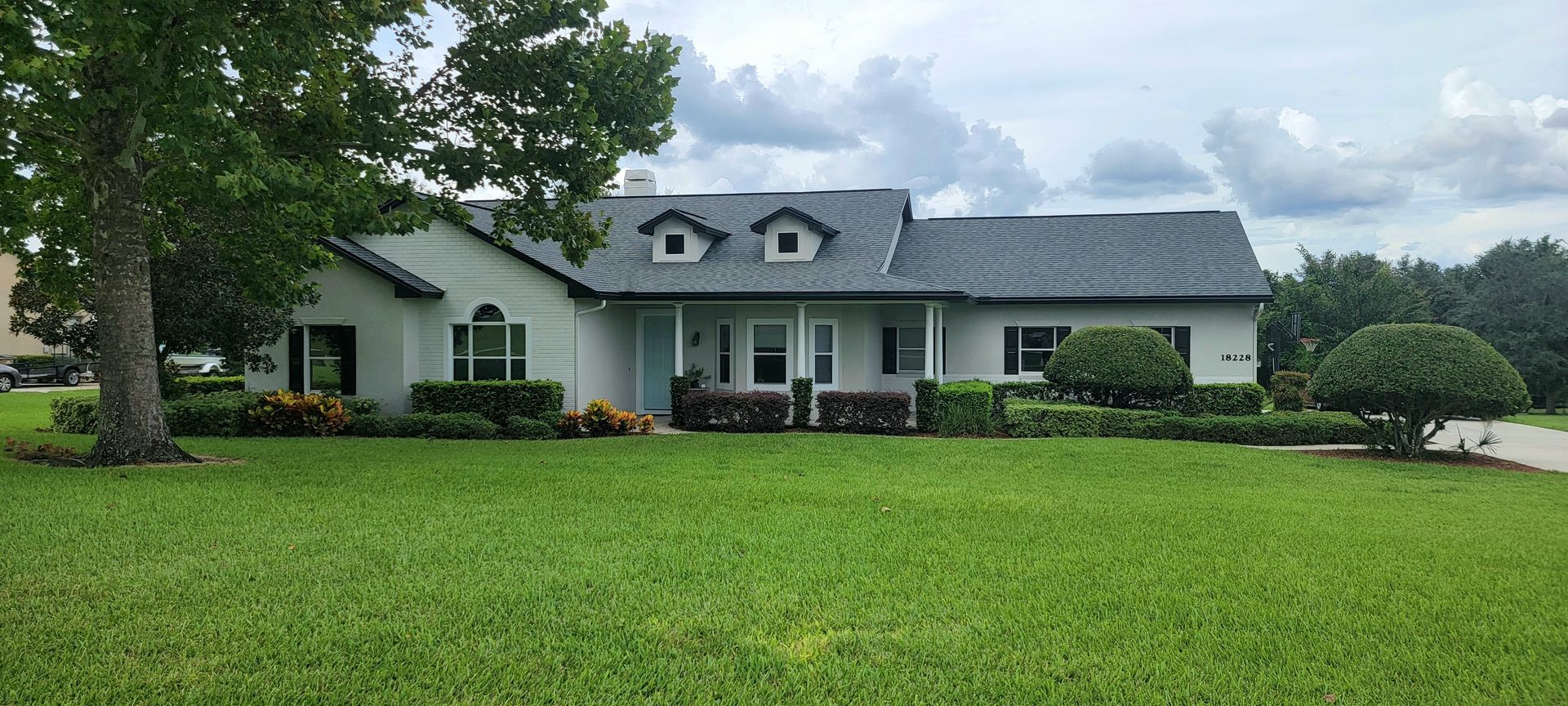 A large white house with a gray roof is sitting on top of a lush green lawn.