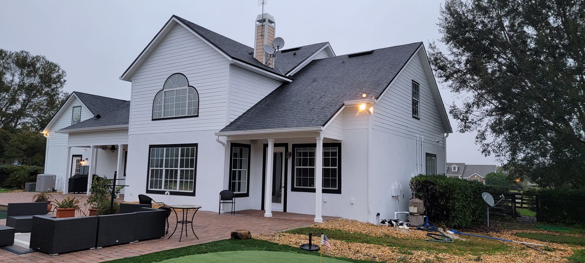 A large white house with a black roof and a putting green in front of it.