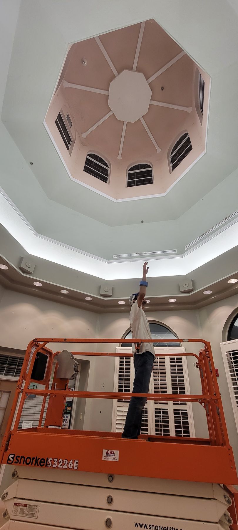 A man is standing on a lift looking up at a ceiling.