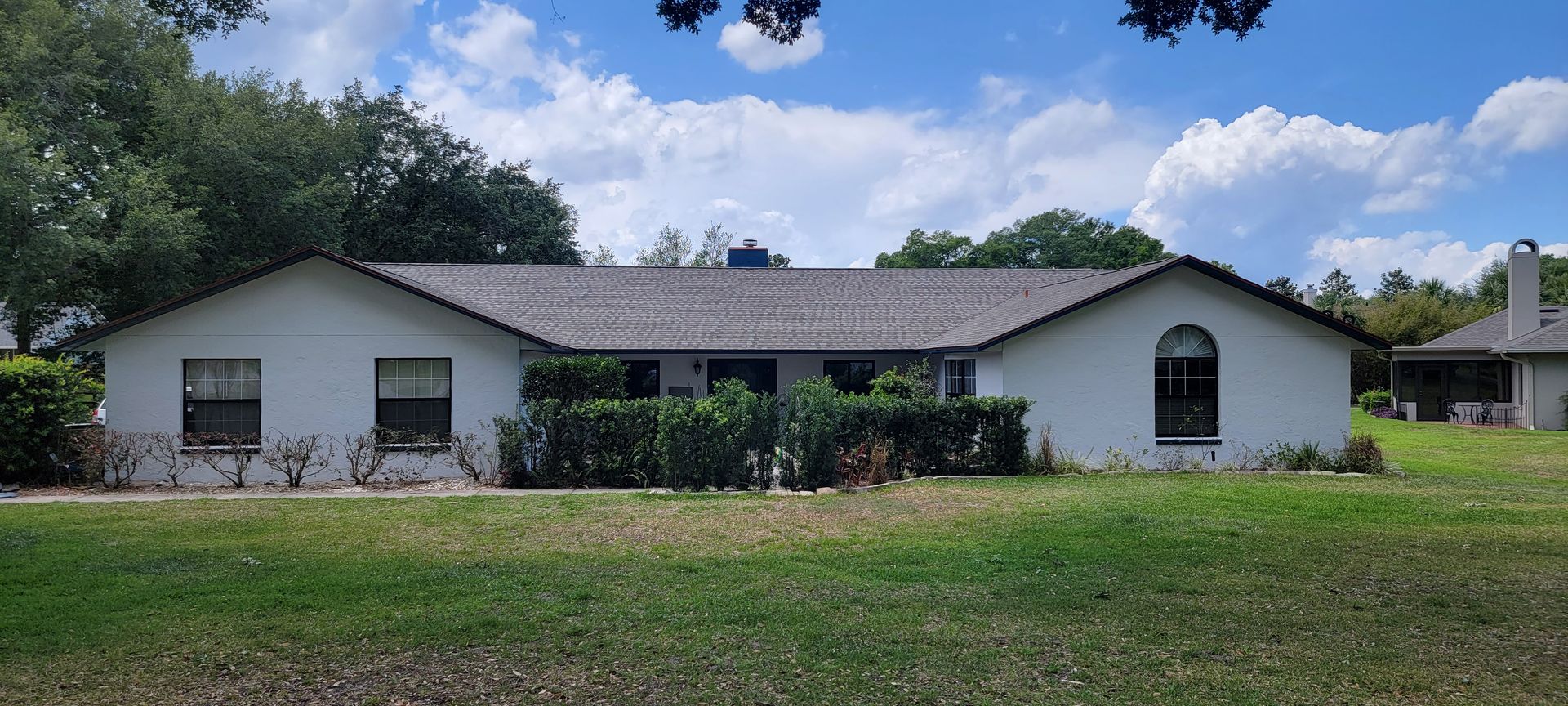 A white house with a gray roof is sitting on top of a lush green field.