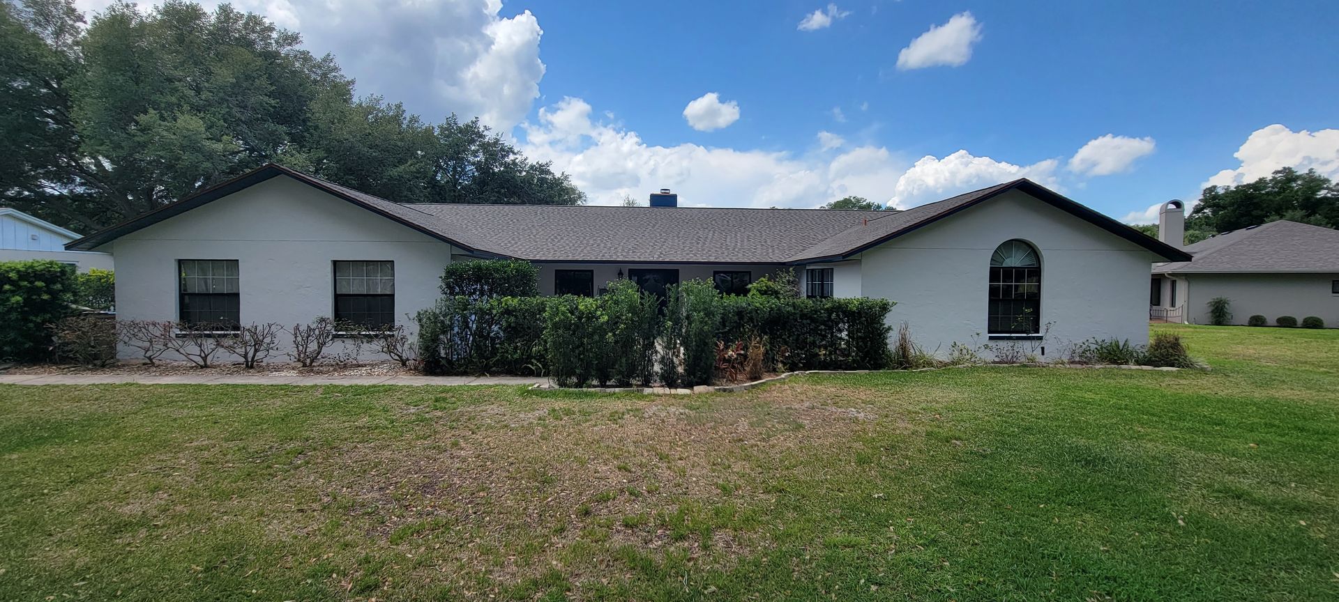 A white house with a gray roof is sitting on top of a lush green field.
