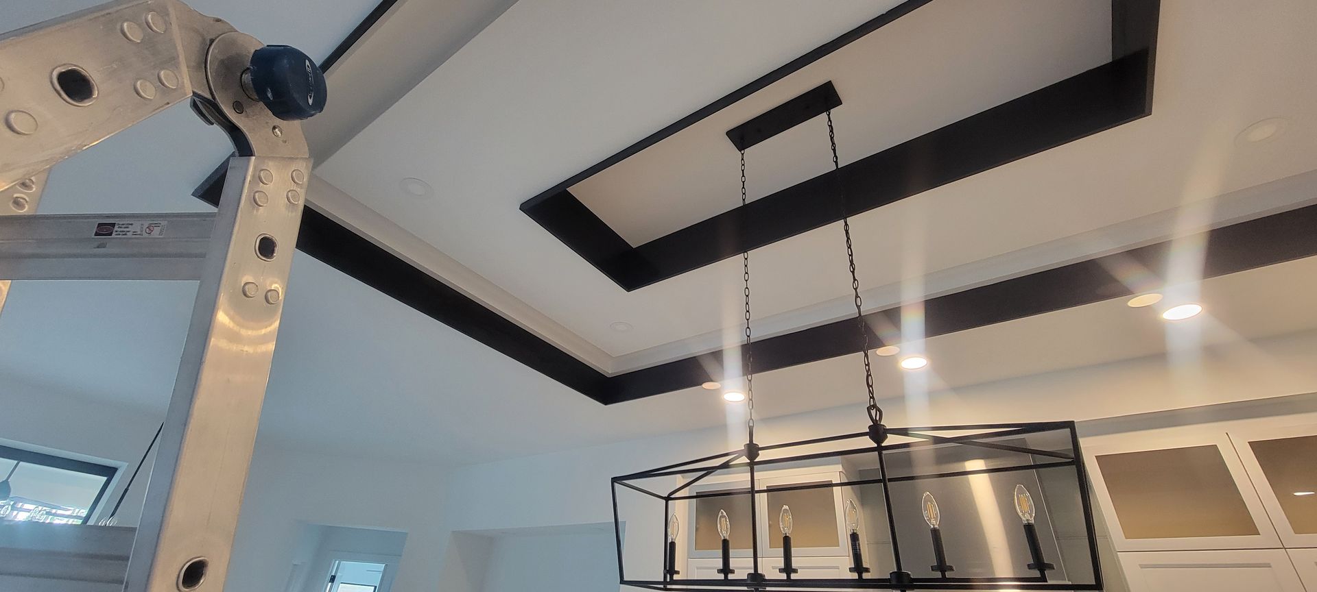 A person is standing on a ladder in a room with a chandelier hanging from the ceiling.