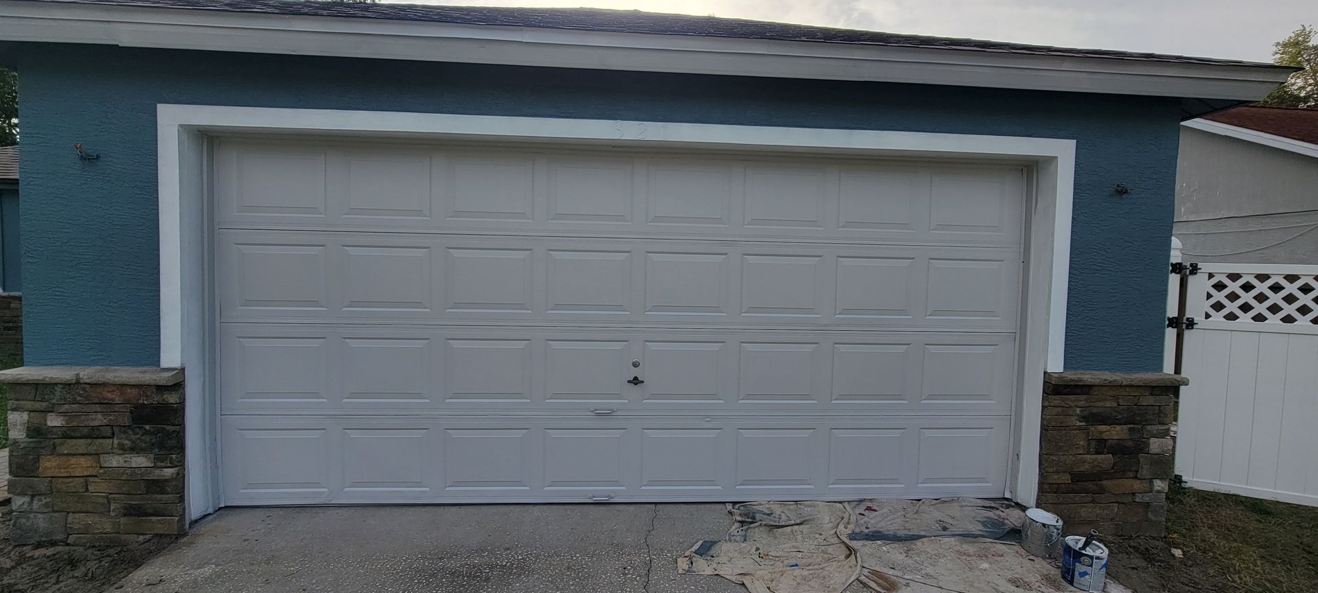 A white garage door is sitting in front of a blue house.