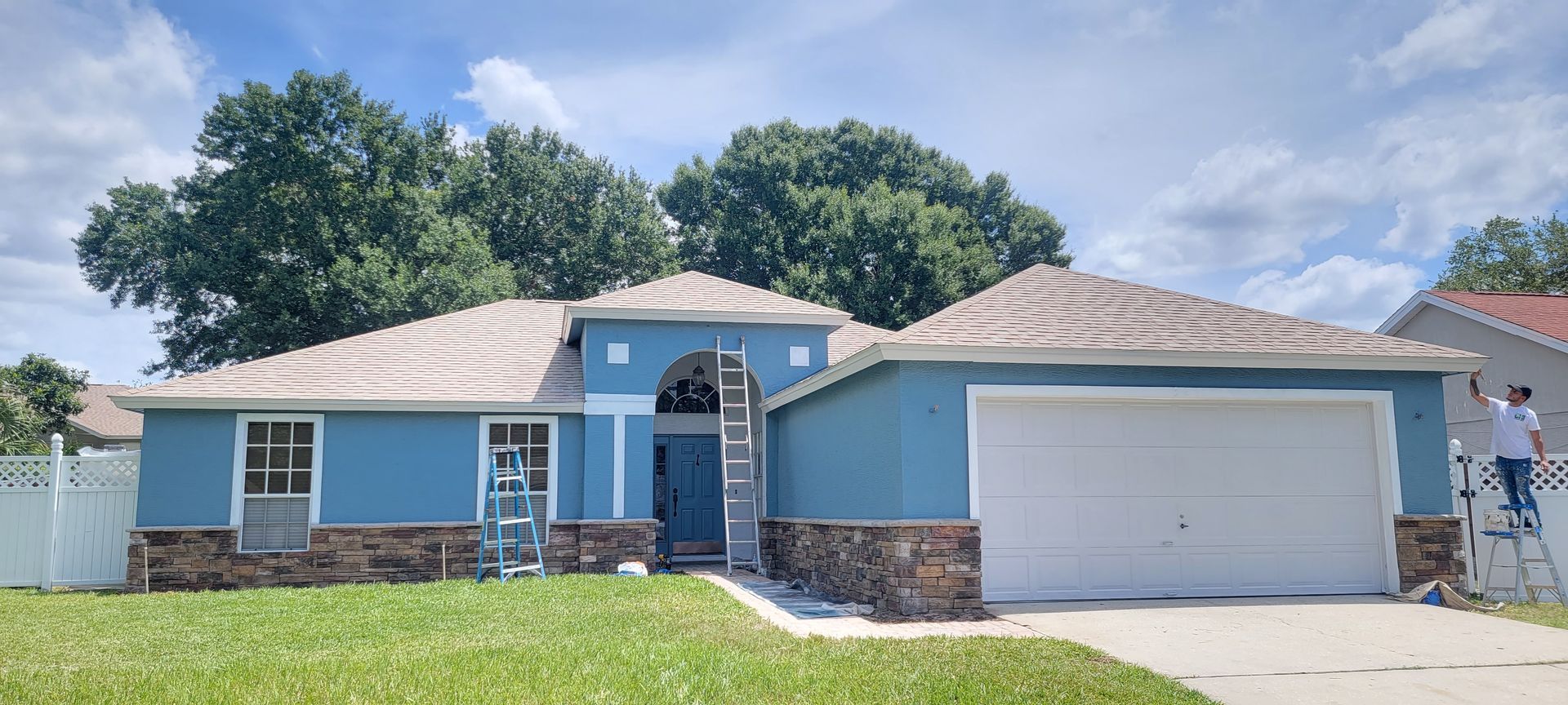 A man is painting the outside of a blue house.