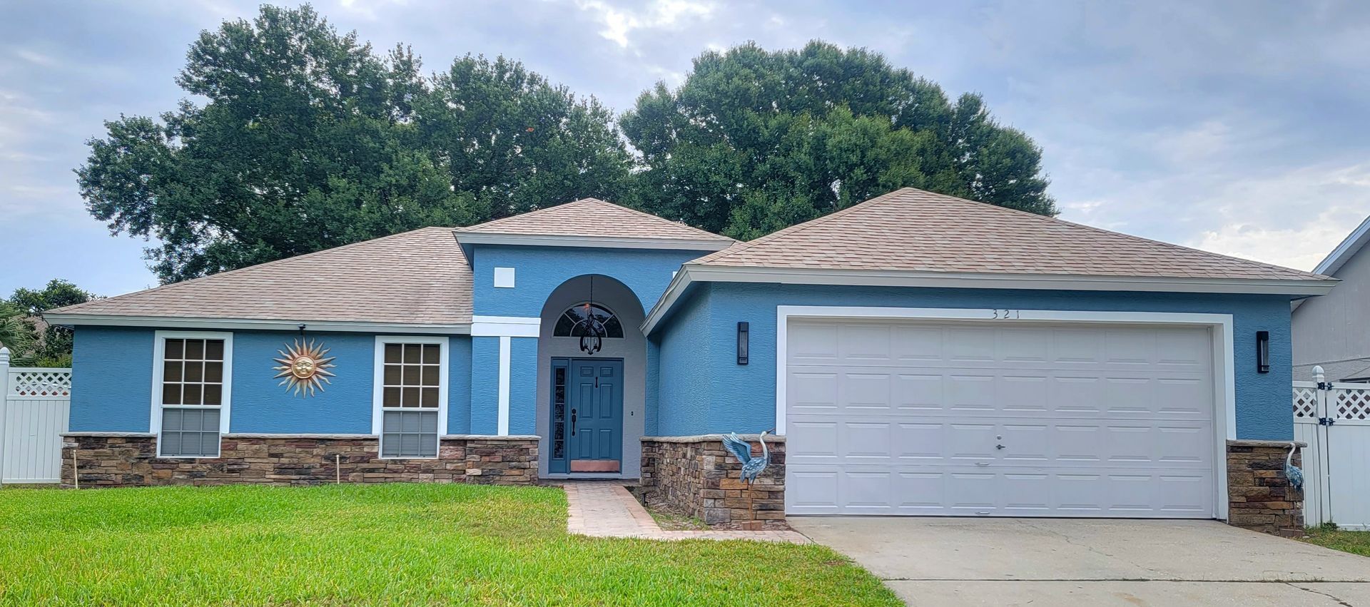 A blue house with a white garage door and trees in the background.