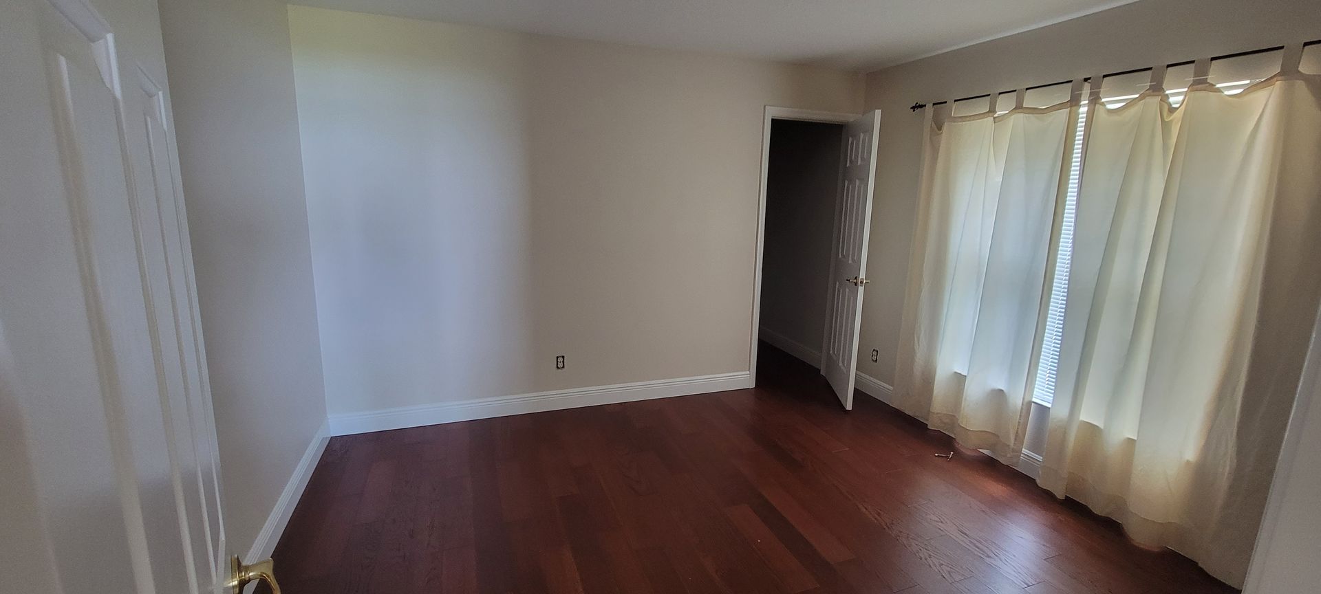 An empty room with hardwood floors and white curtains.