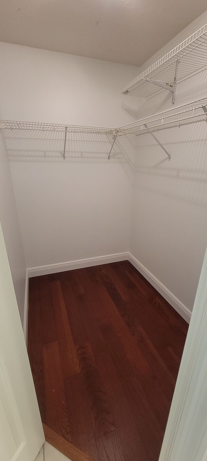 An empty walk in closet with hardwood floors and white walls.