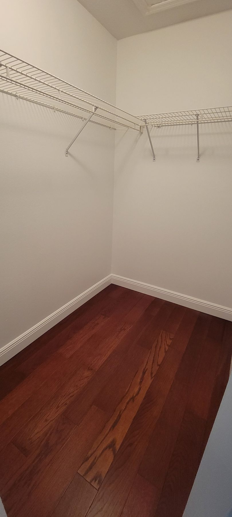 An empty walk in closet with hardwood floors and white walls.