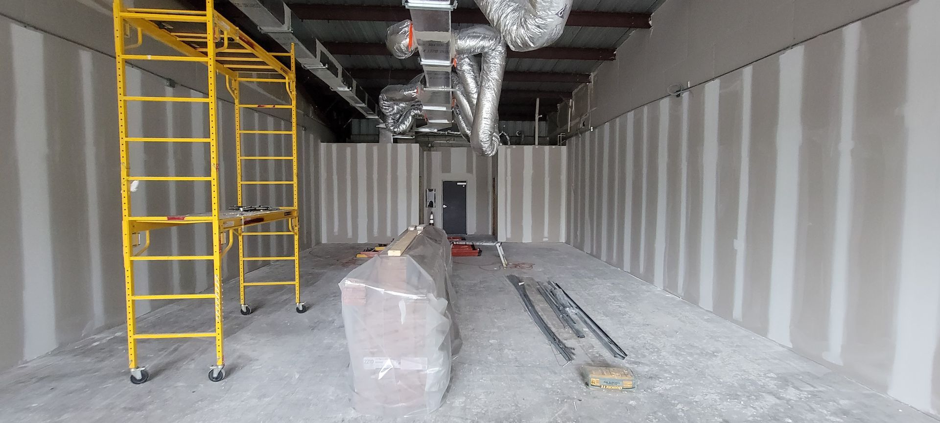A large empty room with scaffolding and ducts hanging from the ceiling.