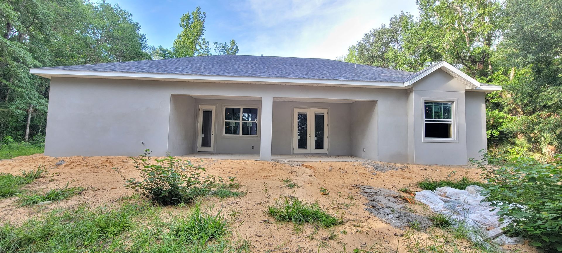 A white house with a blue roof is sitting on top of a dirt field.