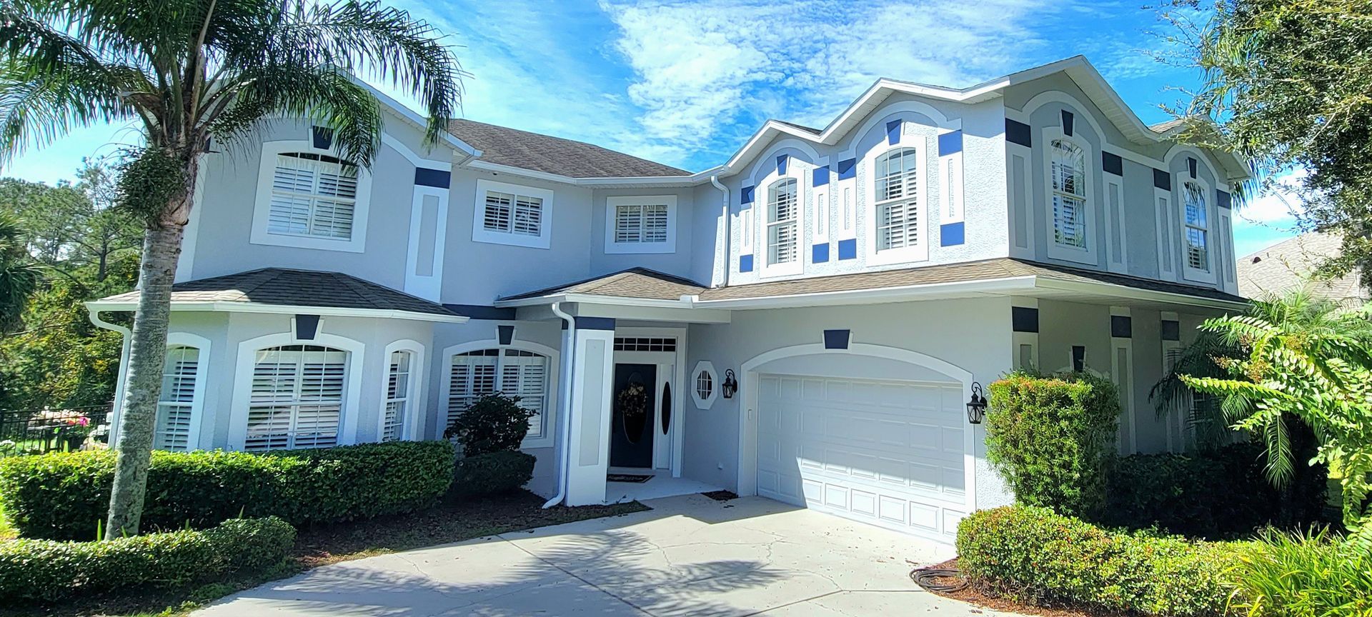 A large white house with blue trim is surrounded by trees and bushes.