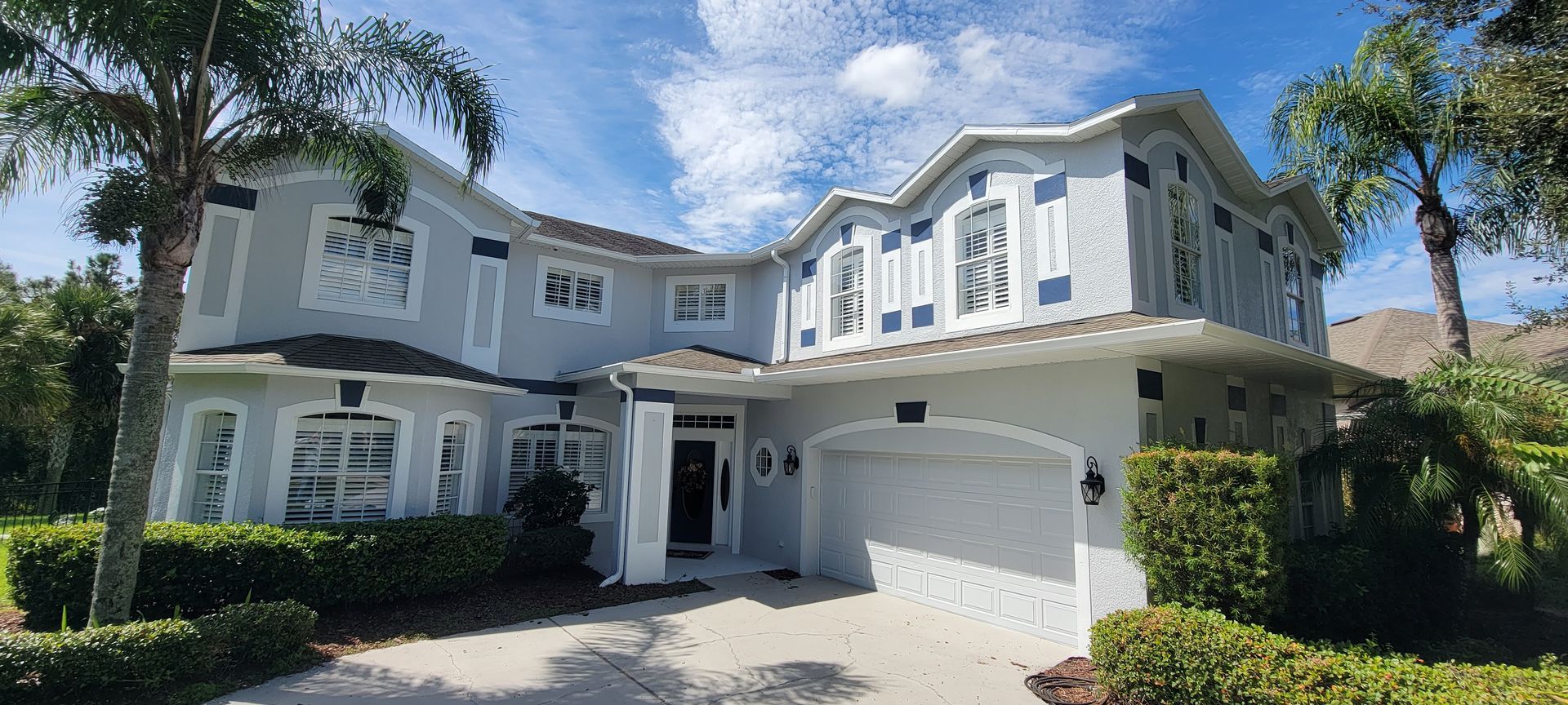 A large white house with a garage and palm trees in front of it.