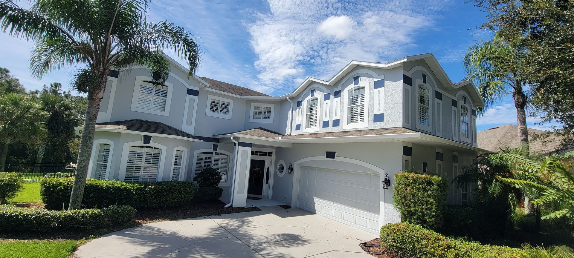 A large white house with a garage and palm trees in front of it.