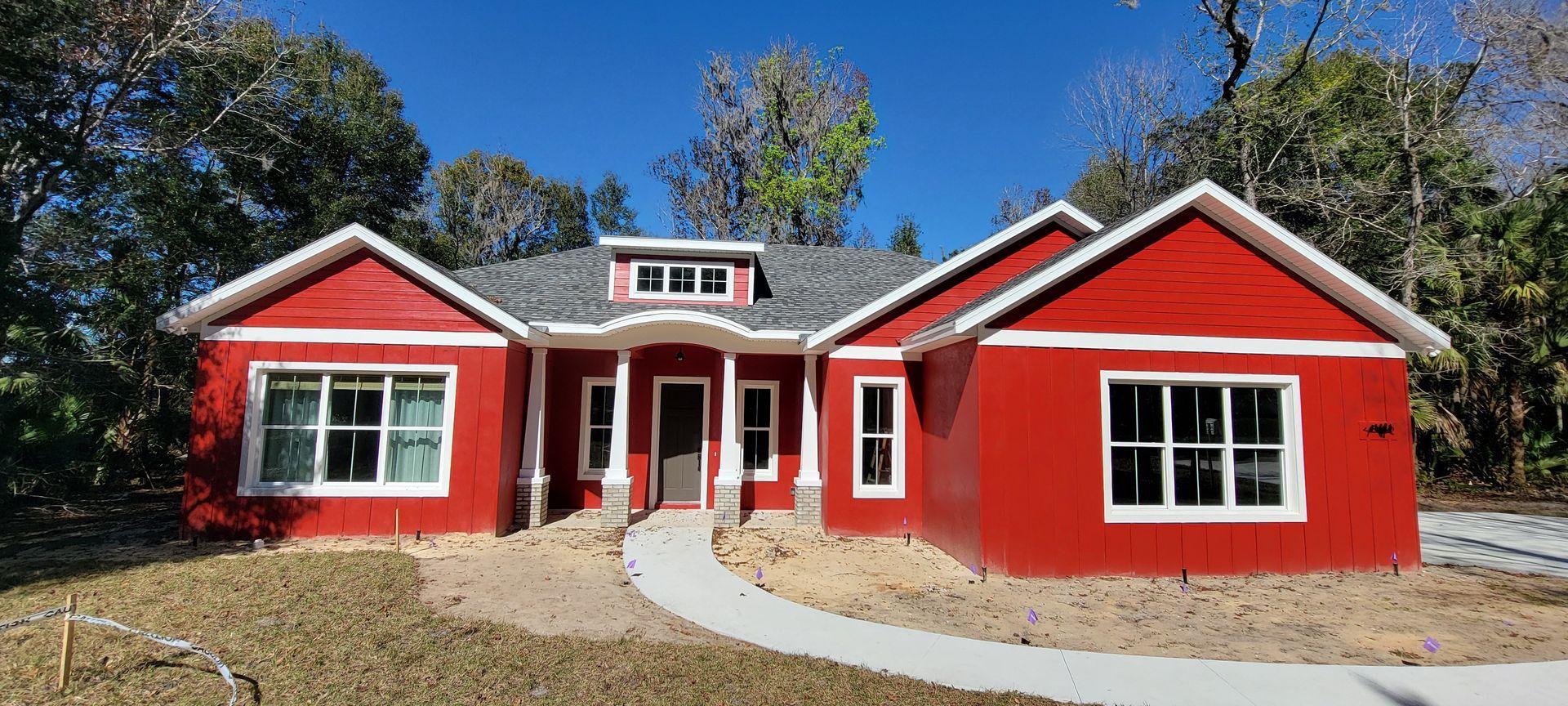 A red house with white trim and windows is surrounded by trees.