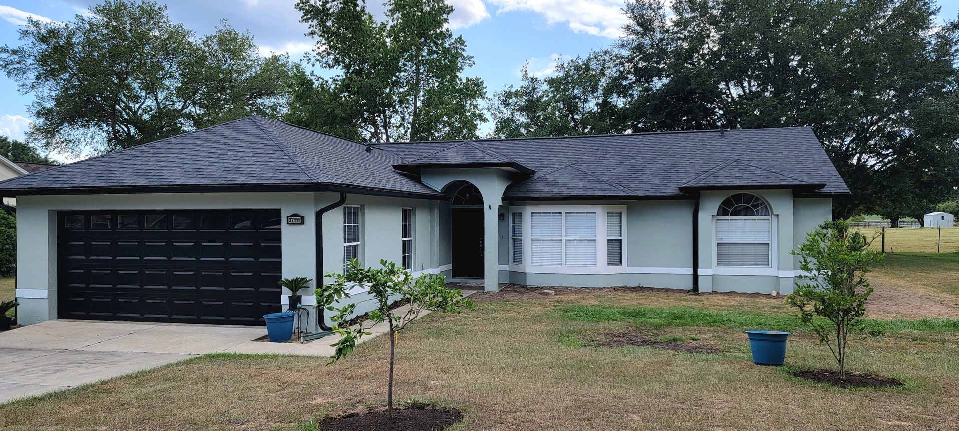 A white house with a black garage door and a tree in front of it.