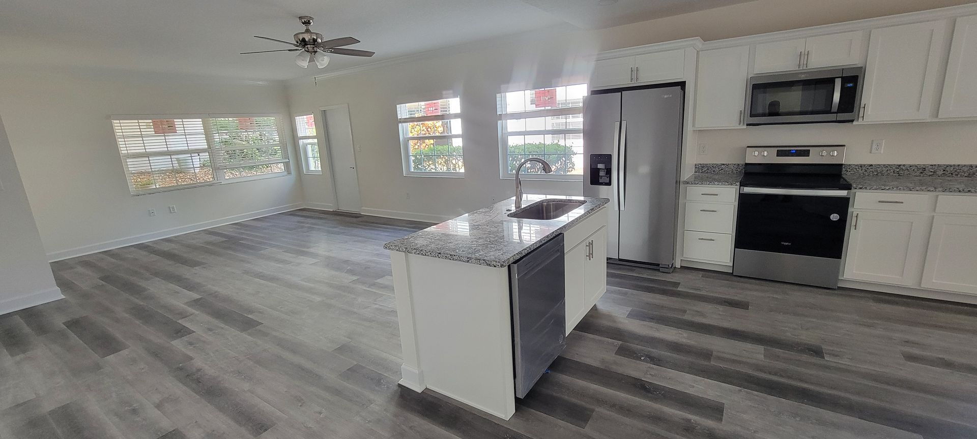 A kitchen with white cabinets , stainless steel appliances , a refrigerator , stove , microwave and sink.
