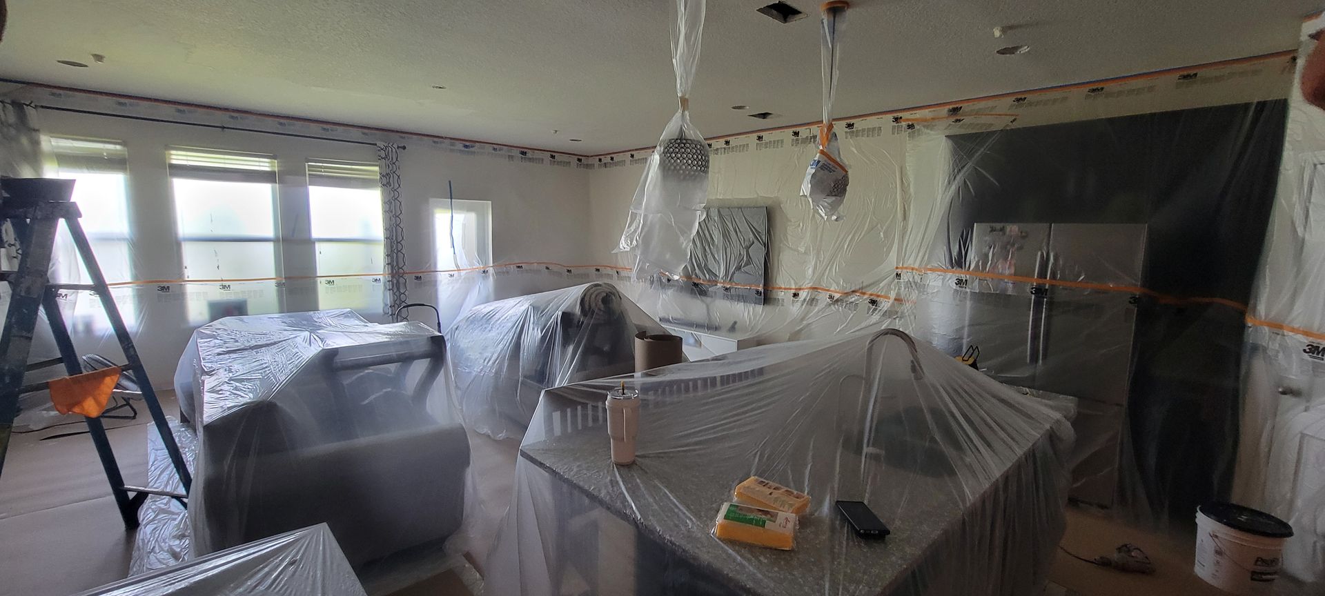 A living room is being painted and covered in plastic wrap.