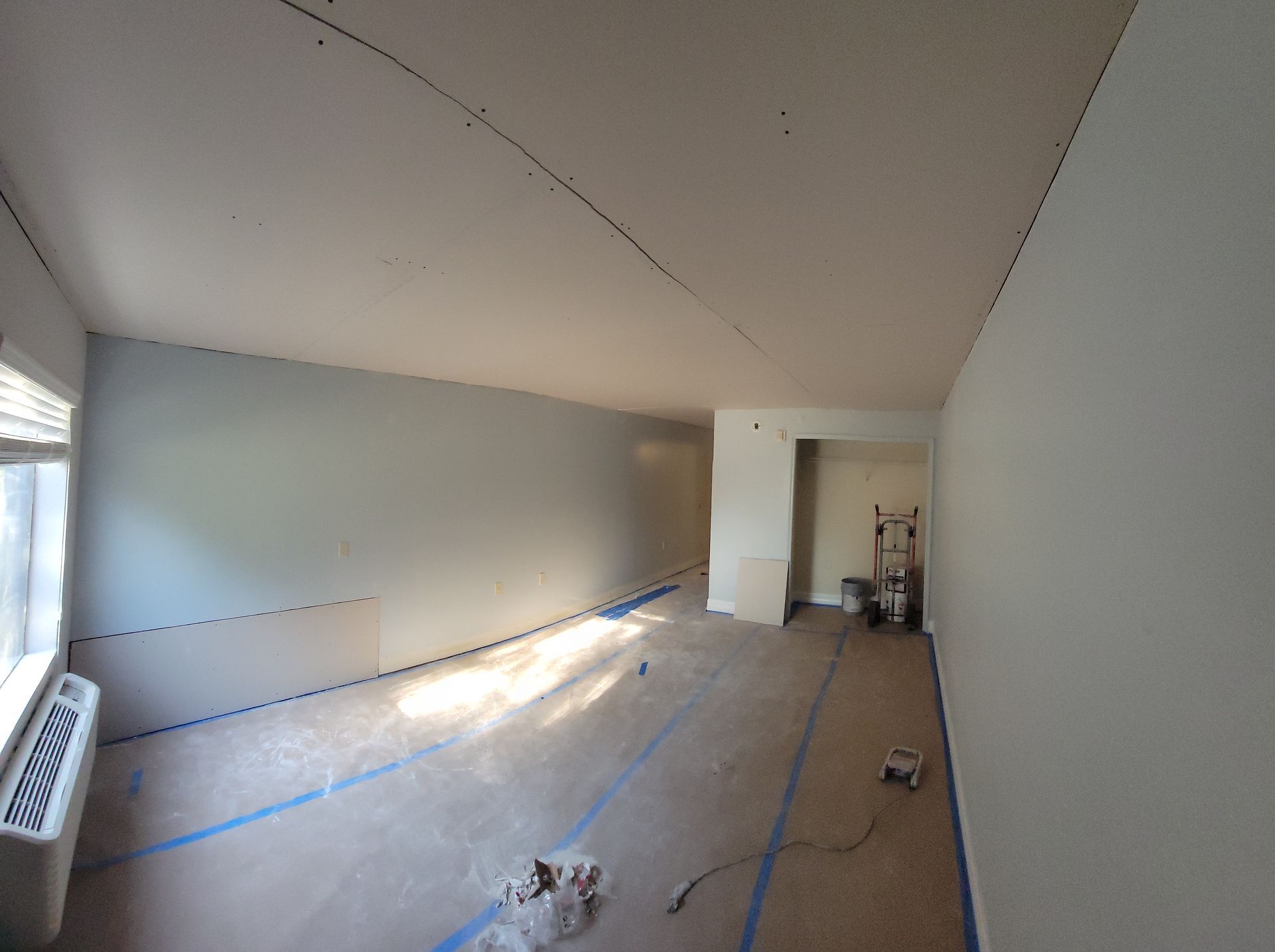 A large room with white walls and blue tape on the floor is being painted.