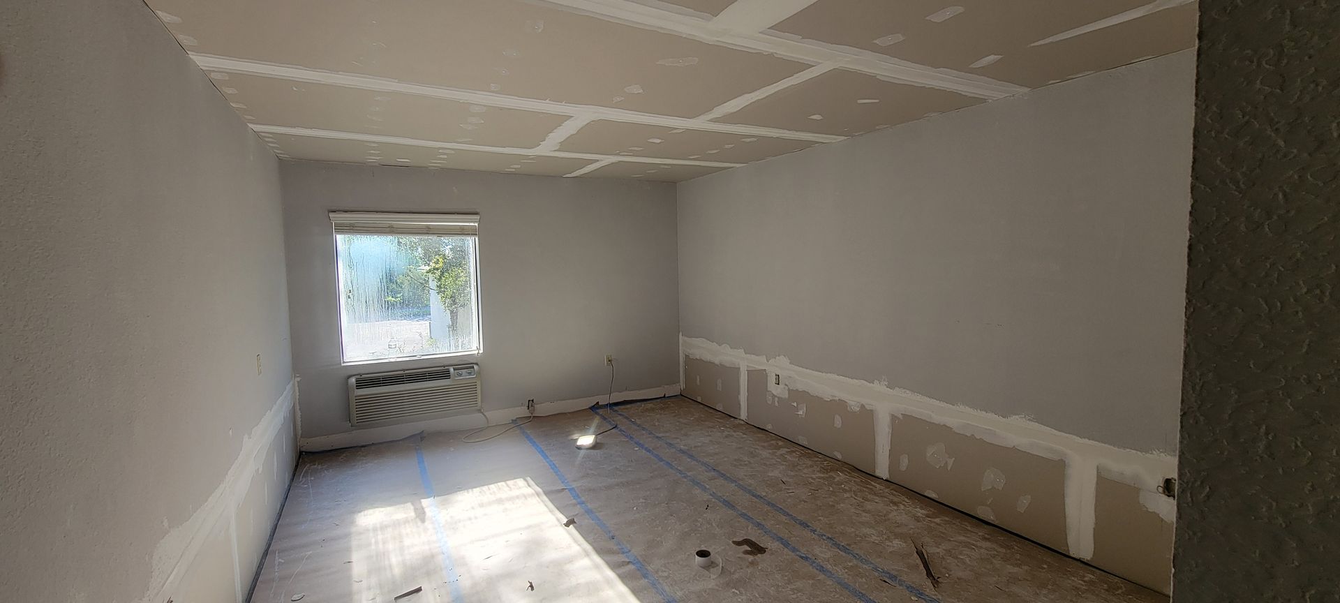 An empty room with a window and drywall on the ceiling.