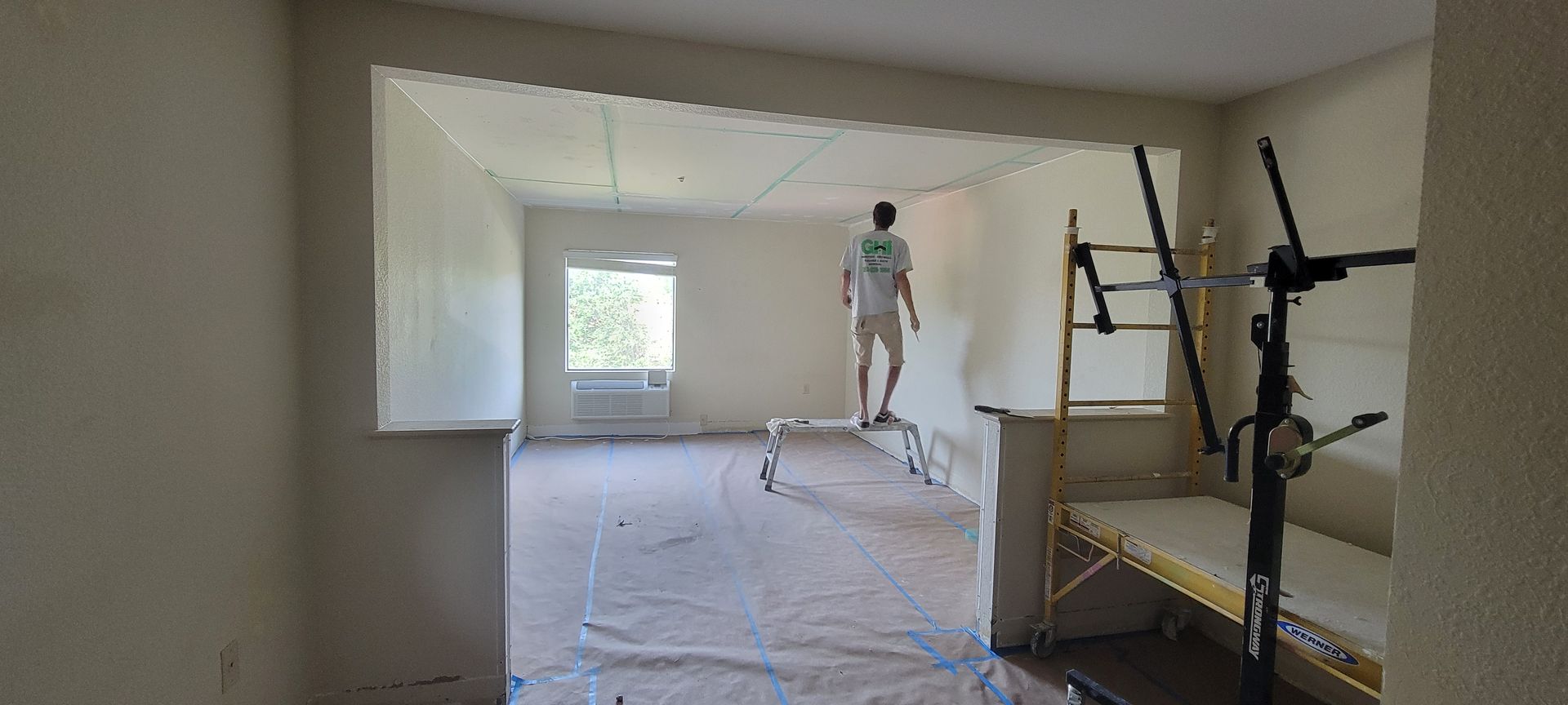 A man is standing on a ladder in an empty room.
