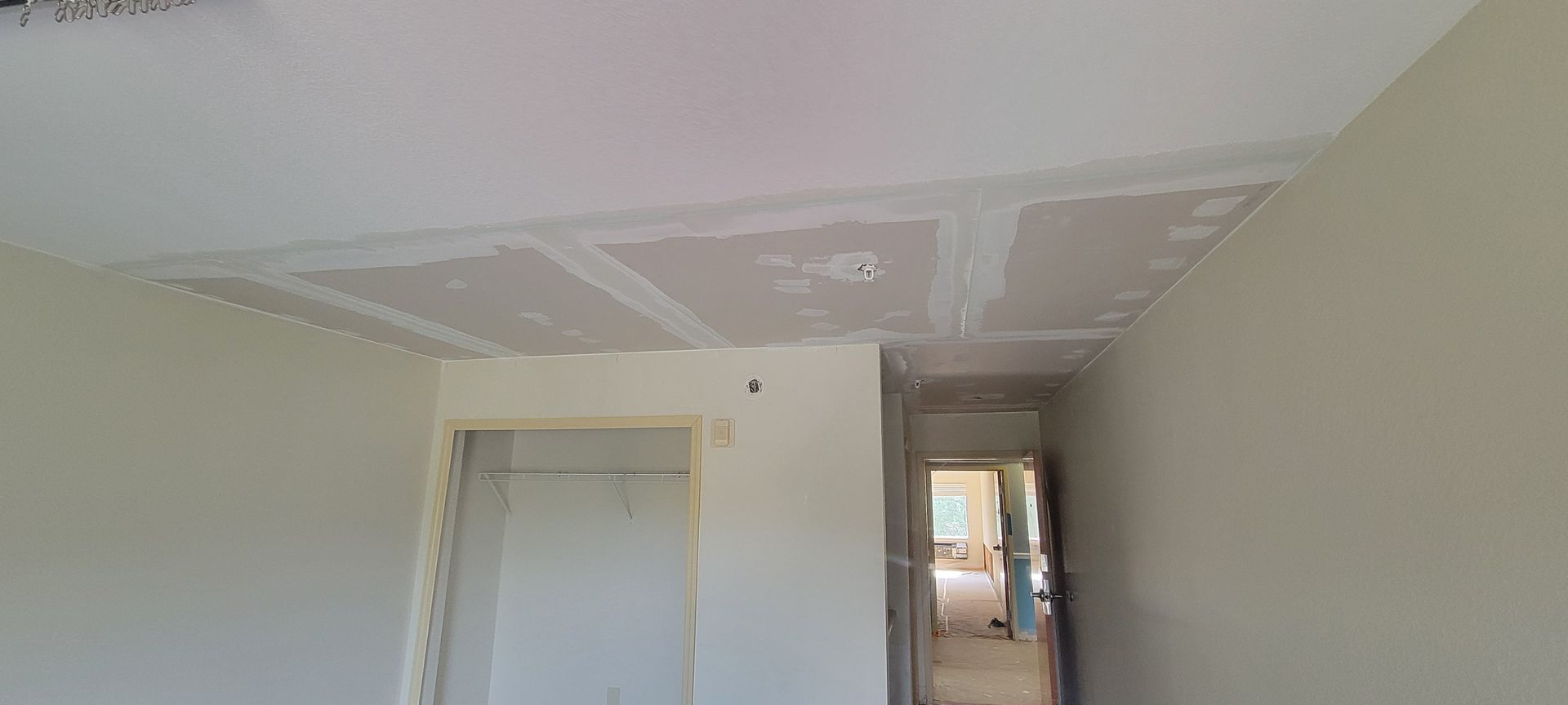 A room with a ceiling that is being painted and a door.