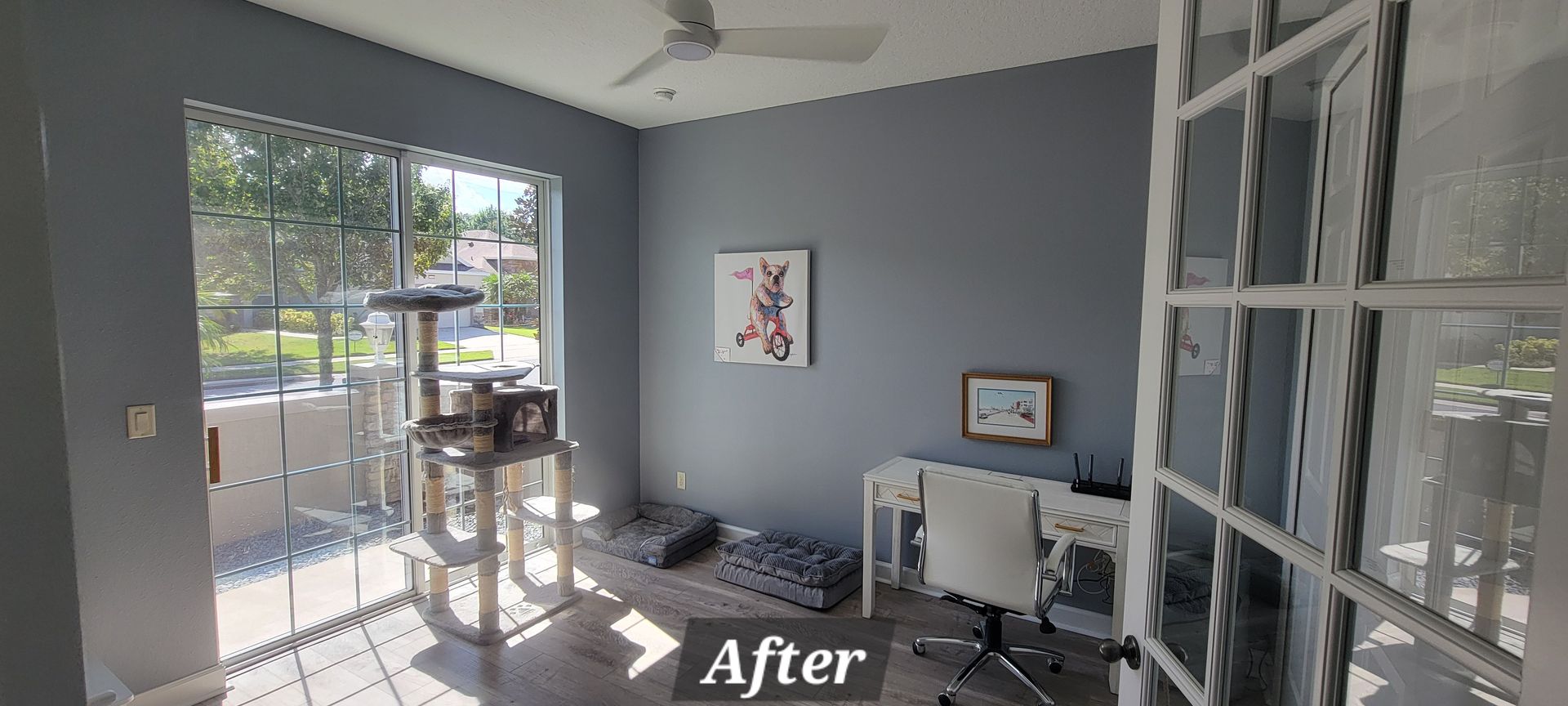 A room with a cat tree , desk , chair and sliding glass doors.