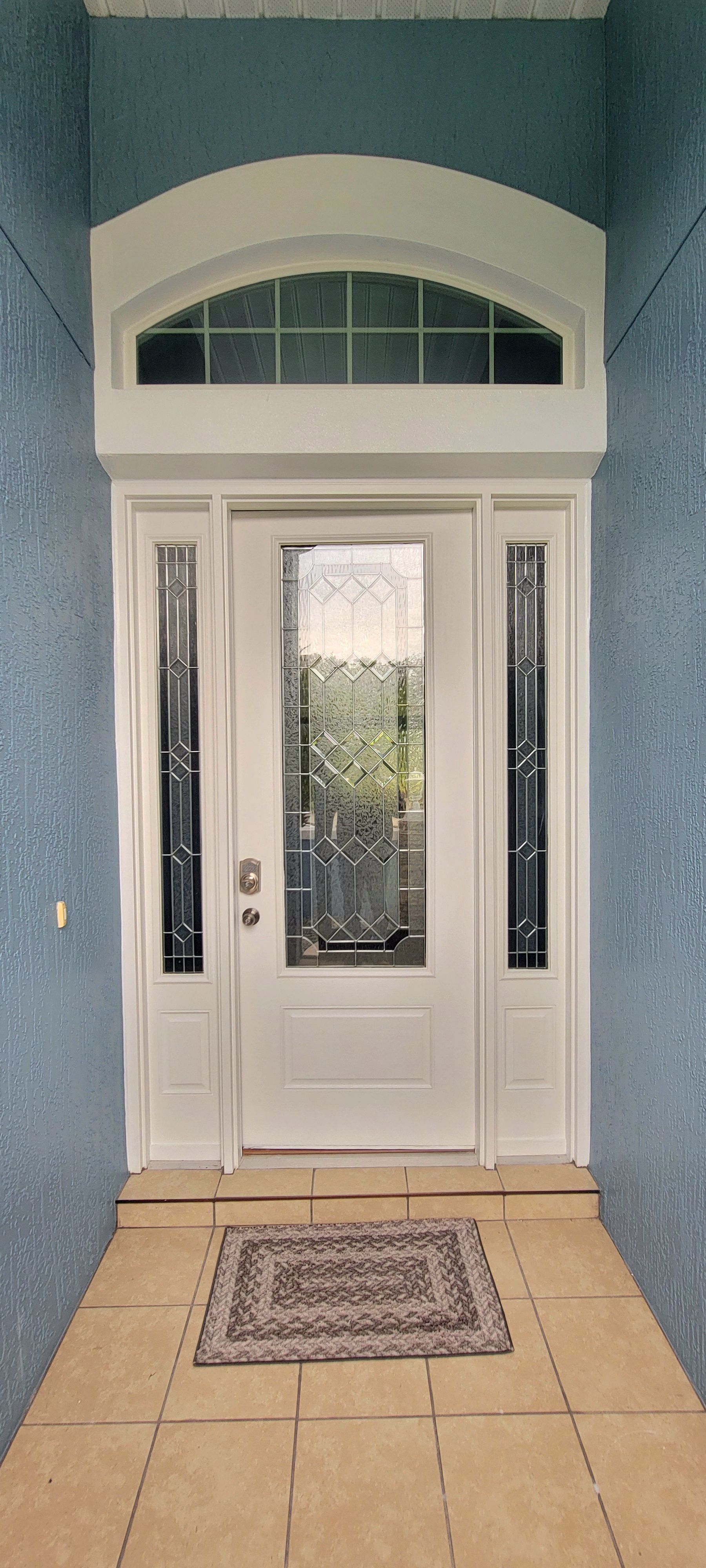 A white front door with a rug in front of it and a blue wall.