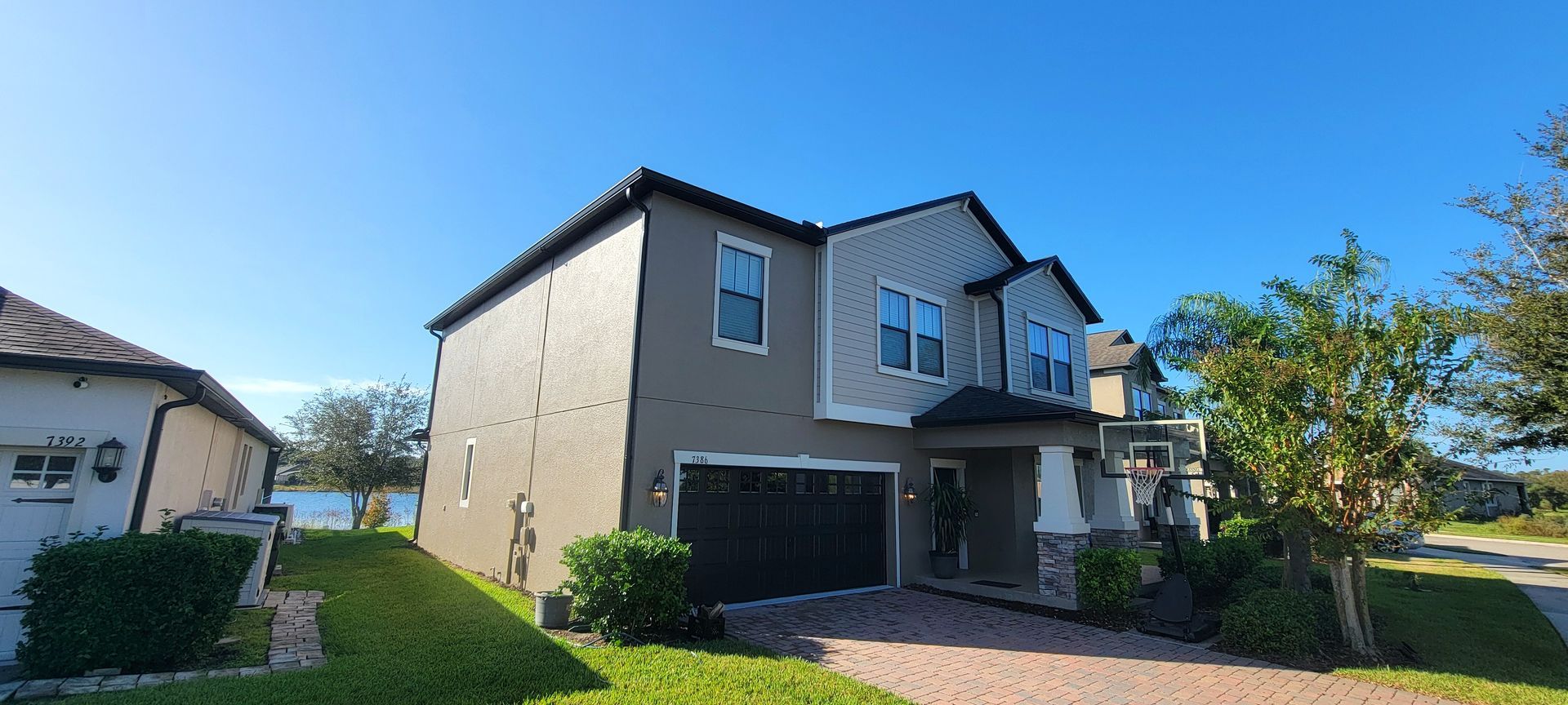 A large house with a large garage is sitting on top of a lush green hill.