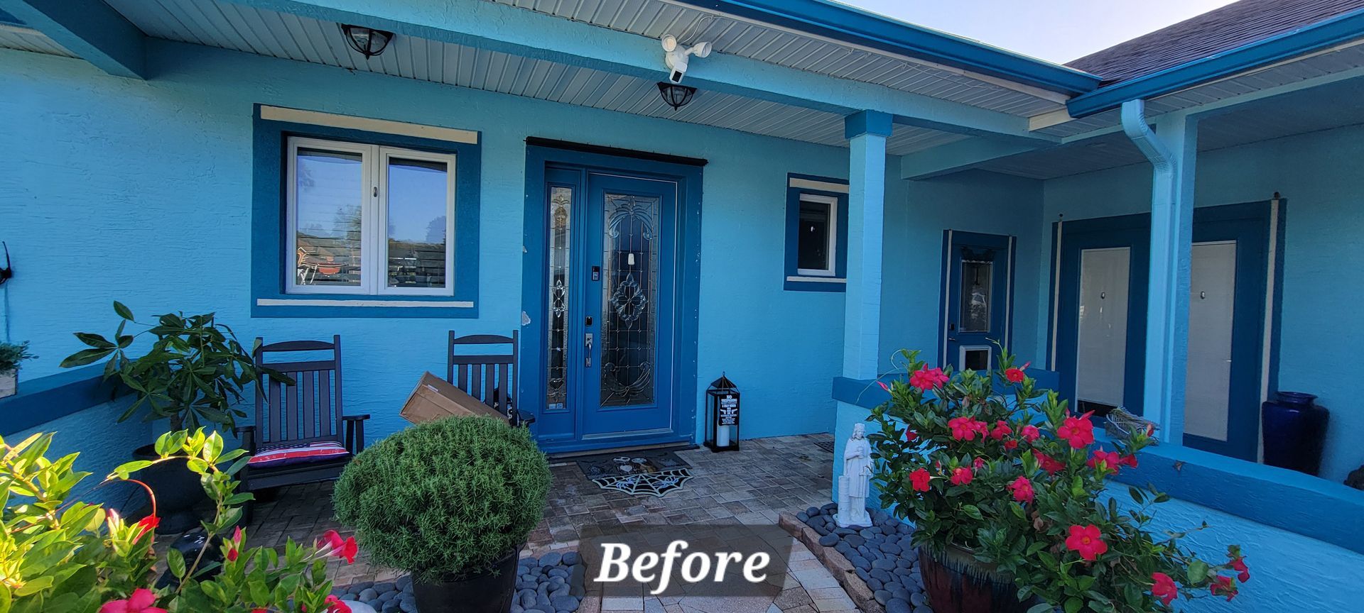 A blue house with a porch and flowers in front of it.