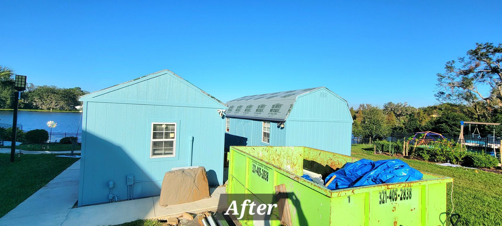 A green dumpster is sitting in front of a blue house.