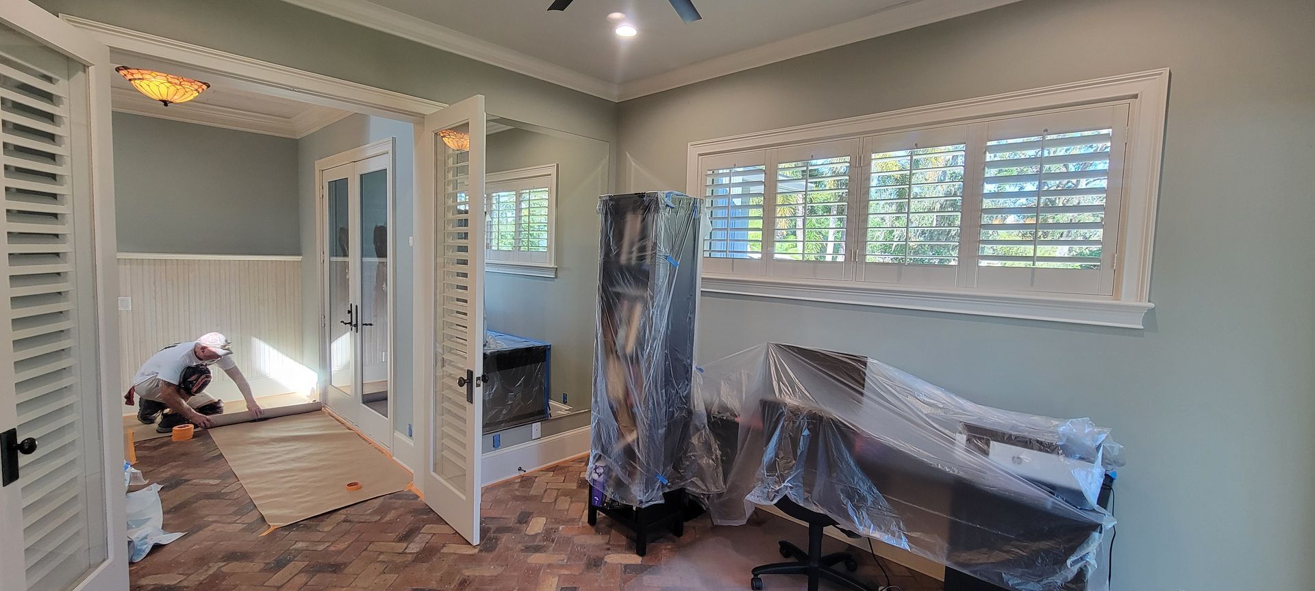 A man is standing in a room with a desk and chairs wrapped in plastic.