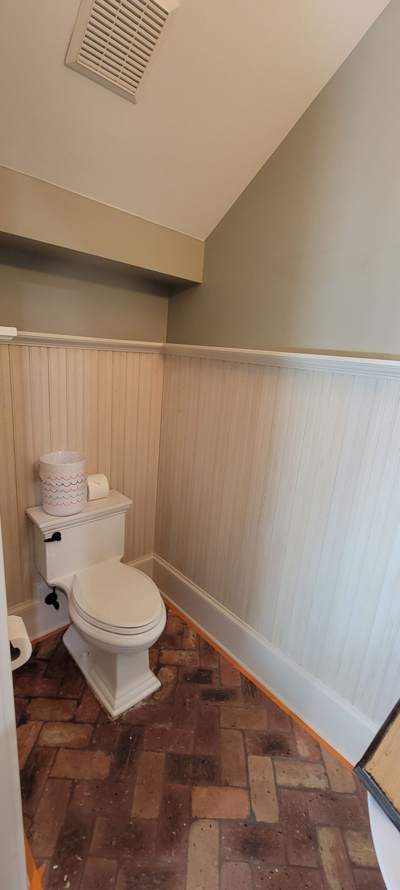A bathroom with a toilet and a brick floor.