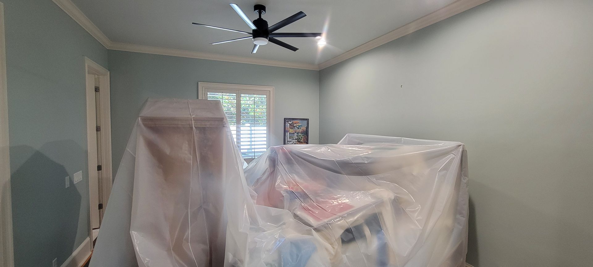 A room with a ceiling fan and a plastic cover on the floor.