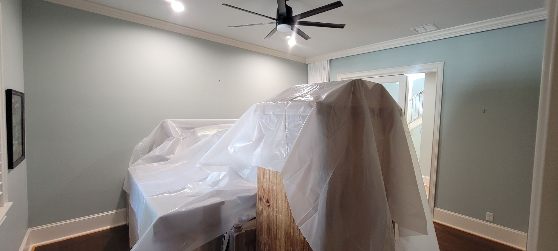 A room with a ceiling fan and a table covered in plastic.