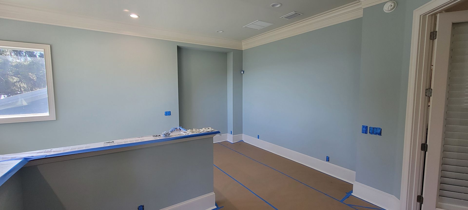 A room with blue walls and white trim is being painted.