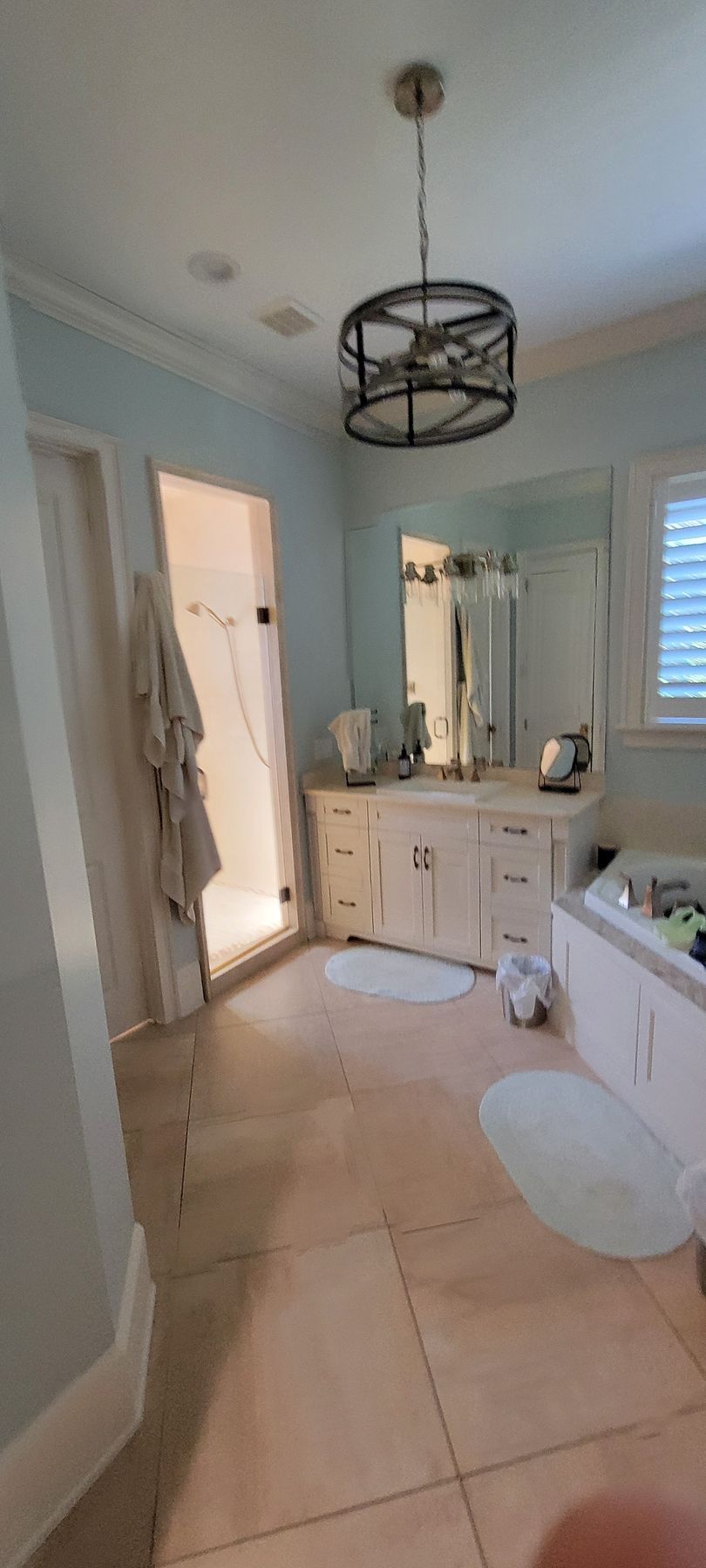 A bathroom with two sinks , a tub , a mirror and a chandelier.