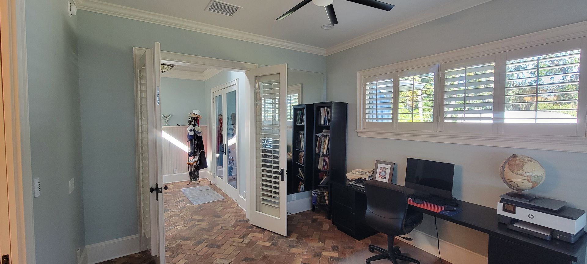 A room with a desk , chair , bookshelf and a ceiling fan.