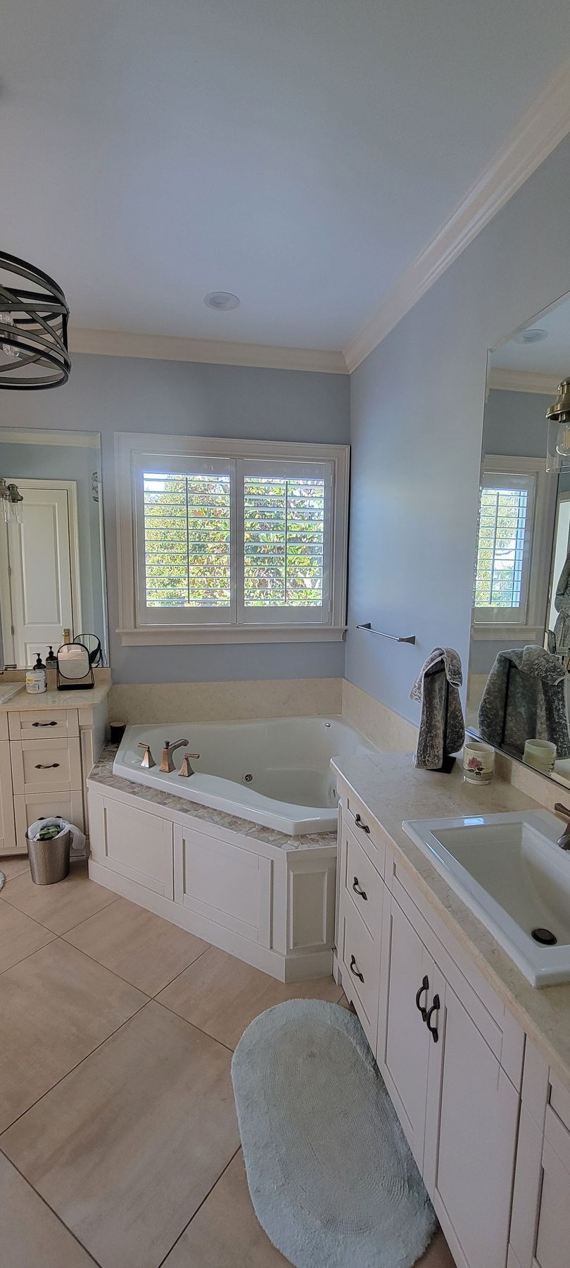 A bathroom with a jacuzzi tub , sink , mirror and window.