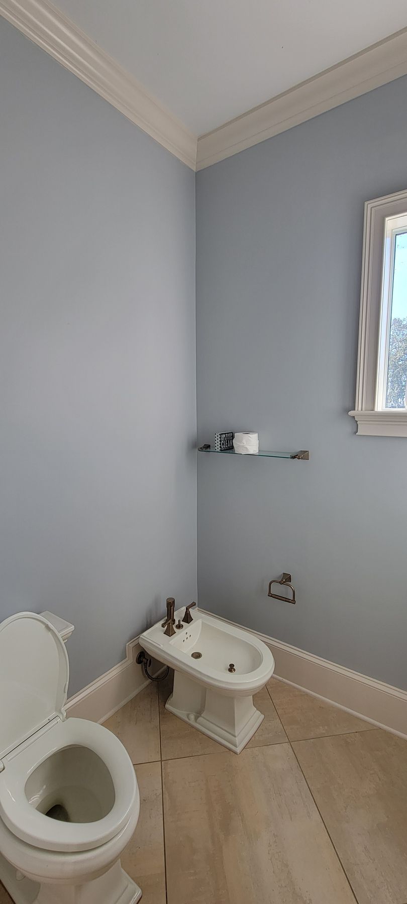 A bathroom with a toilet , bidet and window.