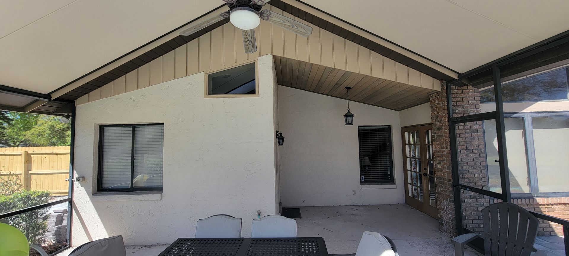 A screened in porch with a table and chairs and a ceiling fan.