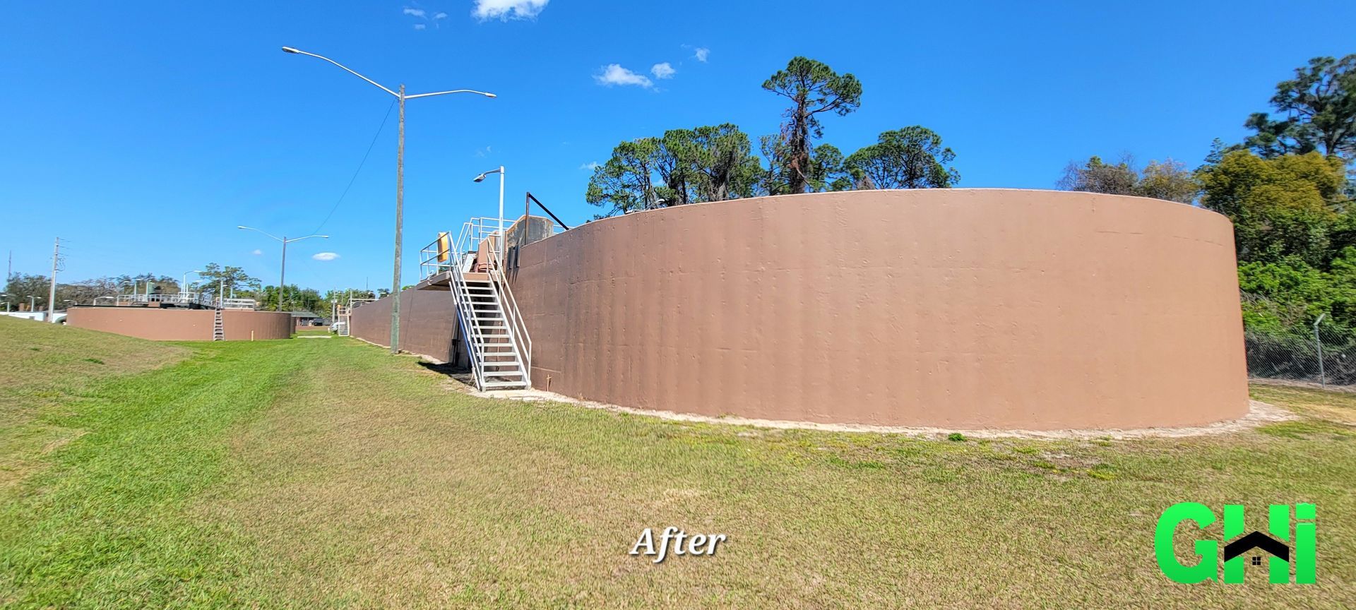 A large water tank with stairs leading up to it is sitting in the middle of a grassy field.